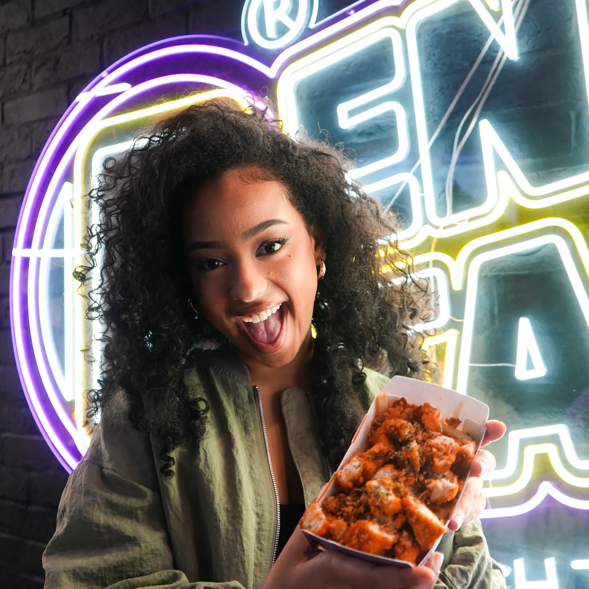 Une cliente rieuse devant le néon Enjoy Tacos, une barquette de poulet croustillant à la main