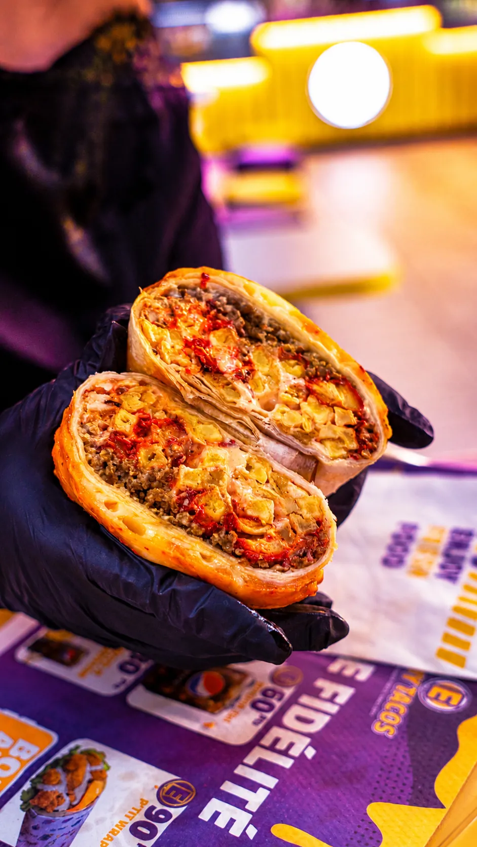 Un tacos coupé en deux tenu à deux mains, garniture généreuse visible à l’intérieur